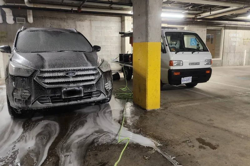 A Ford Escape being foamed in an underground parkade, kei truck parked behind.